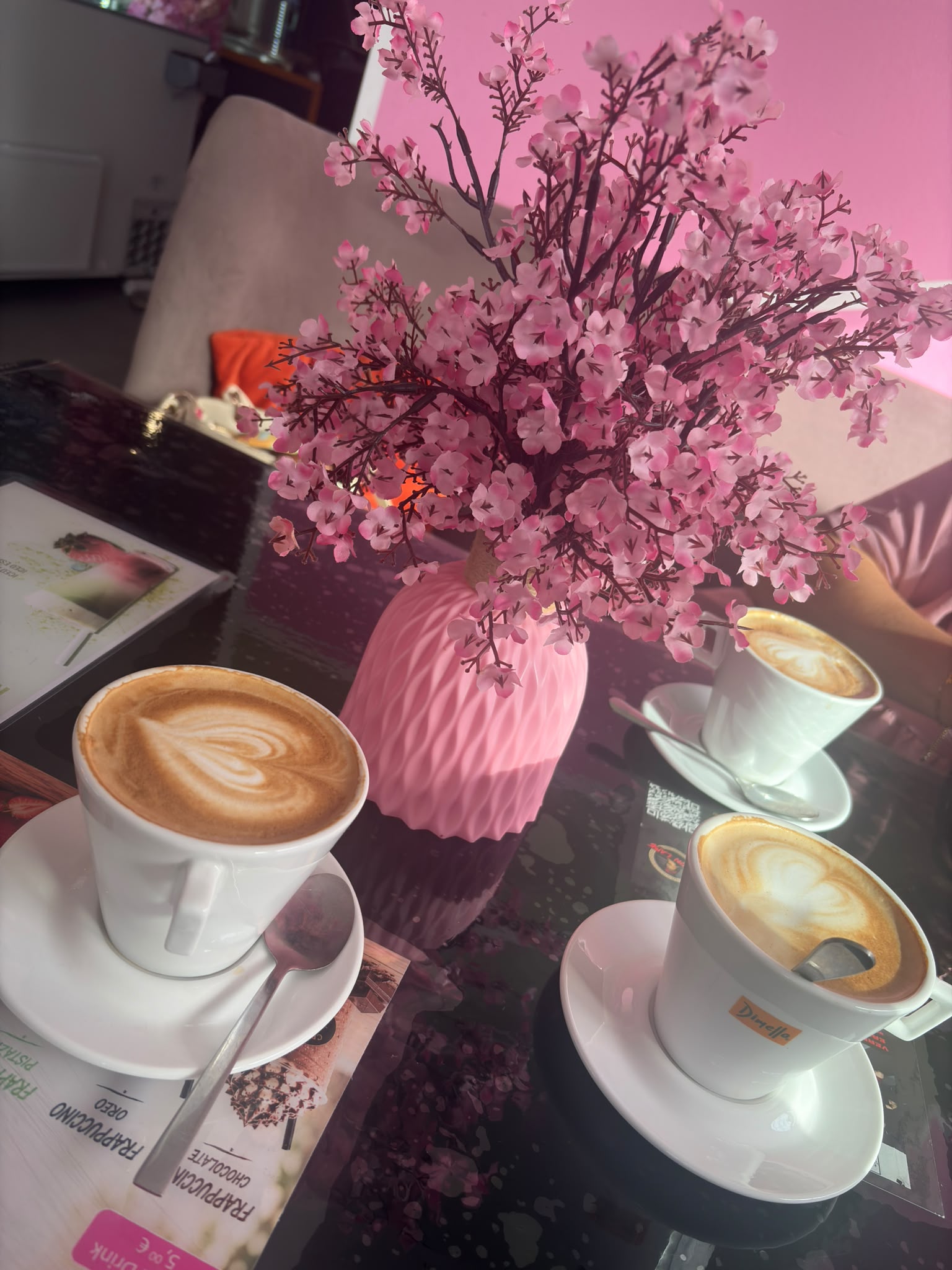 Cappuccino mit Latte Art neben pinker Blumenvase